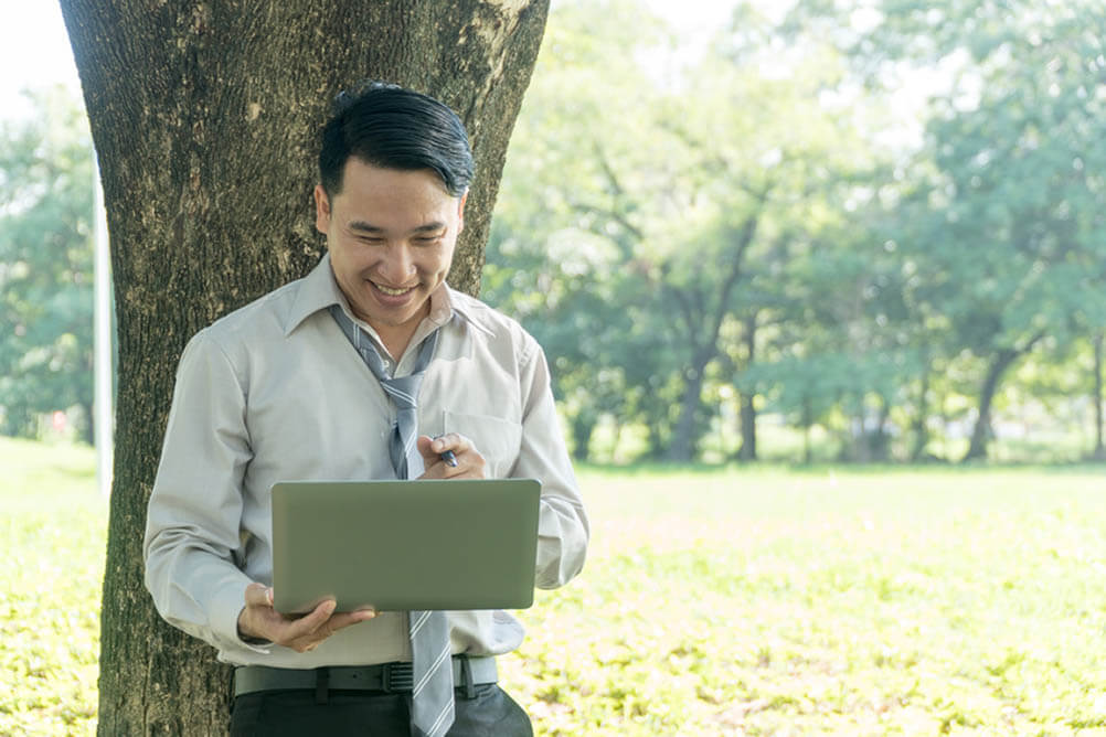 Man smiles while looking at laptop outdoors
