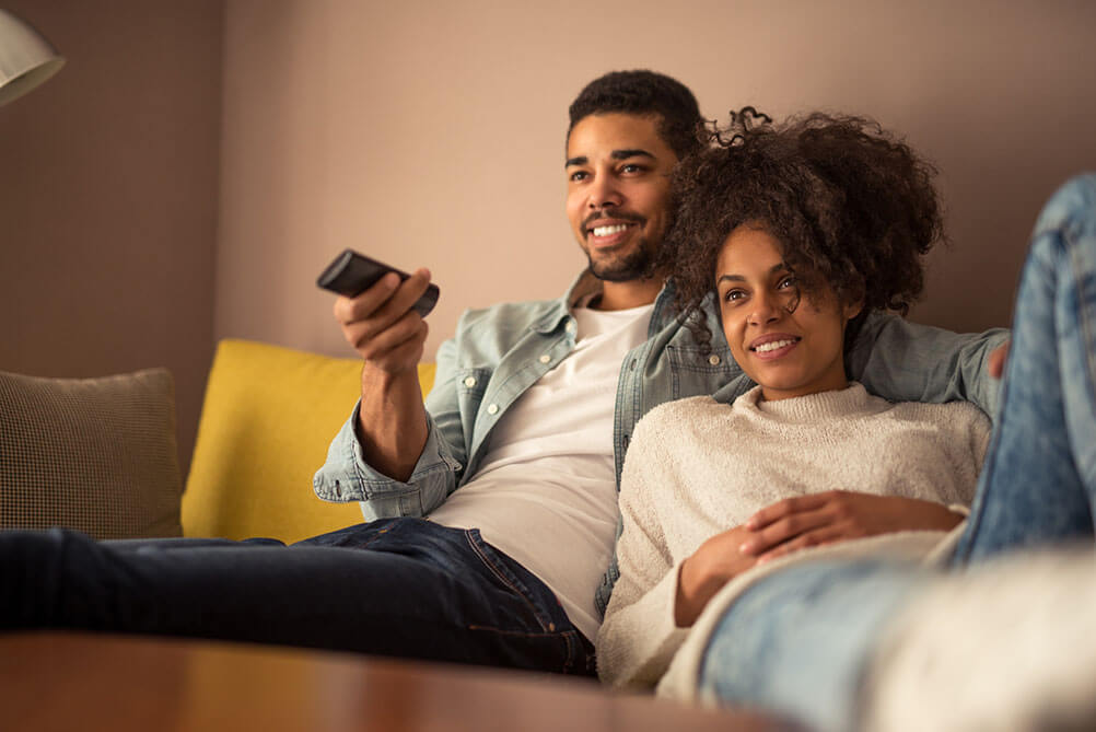 Couple sitting on sofa watching TV show and smiling