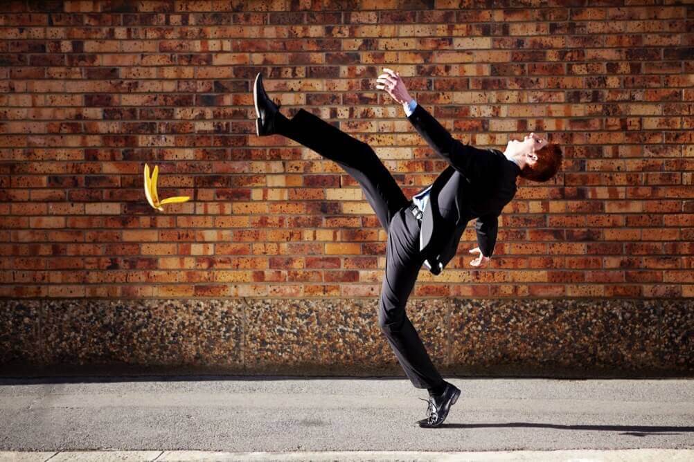 Man in a suit slipping on a banana skin in front of a brick wall