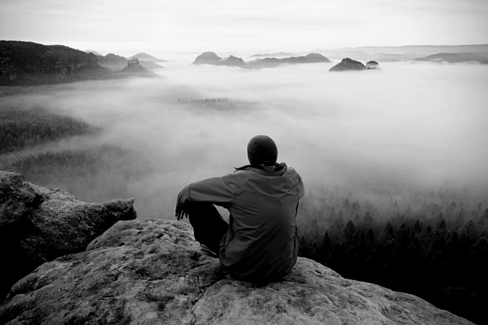 Man sitting on top of a mountain overlooking the clouds