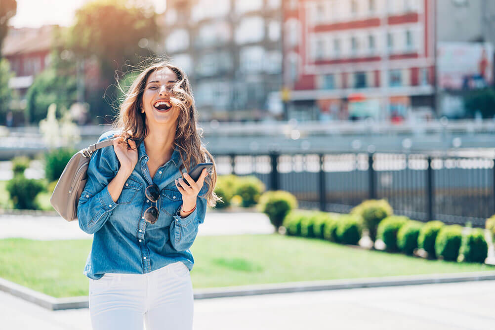 Woman laughing in park as she holds her phone