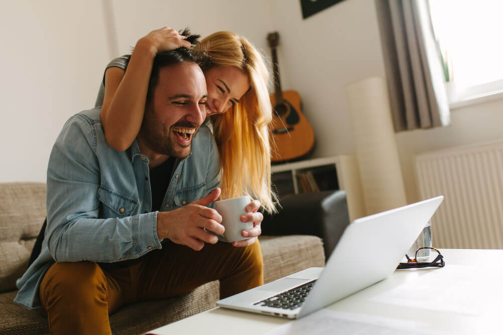 A couple celebrate winning money from an online lottery while looking at their laptop