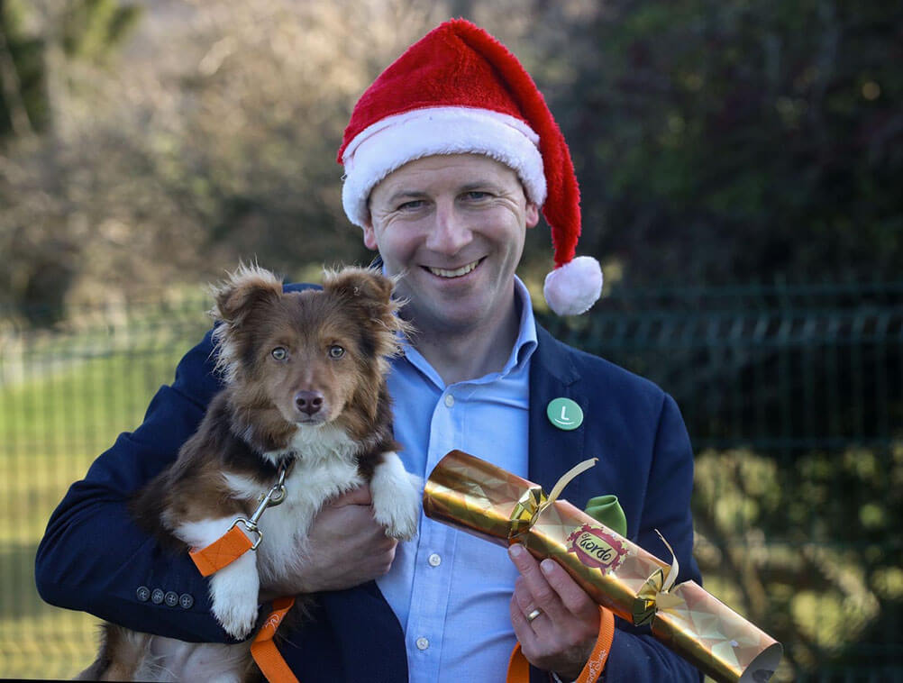 Lottoland Ireland Manager holds a dog from the DSPCA and a Christmas cracker with the El Gordo lottery logo