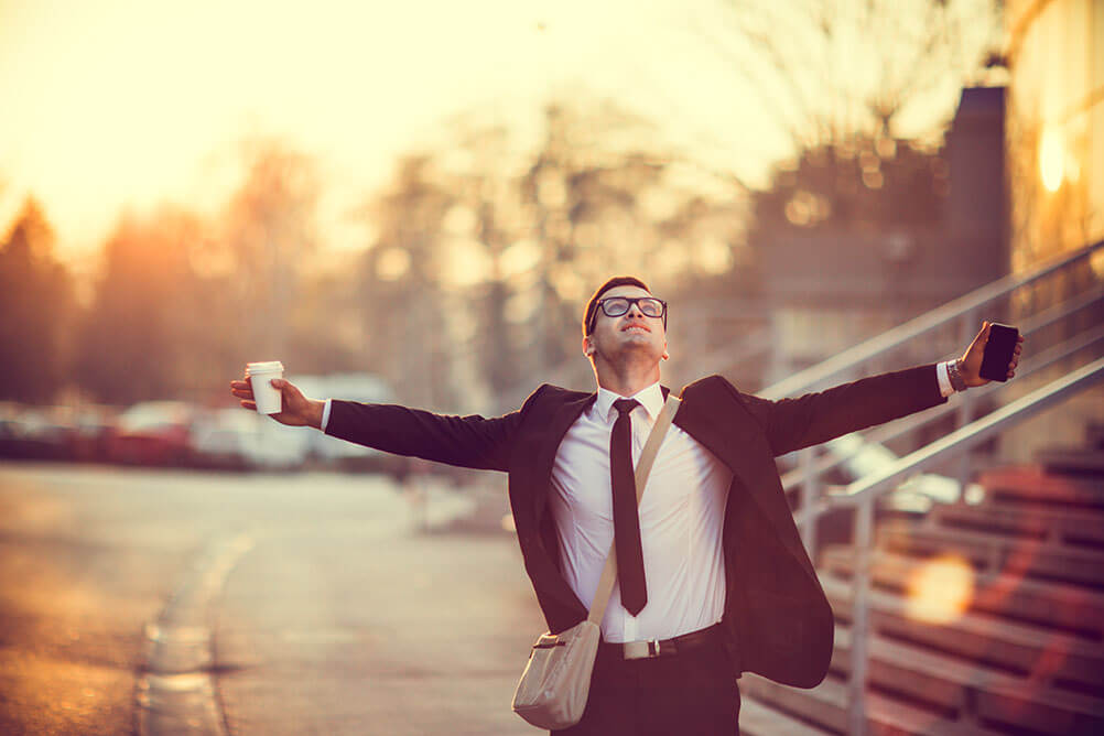 A man in a suit spreads his arms in joy after finding a winning lottery ticket on the street