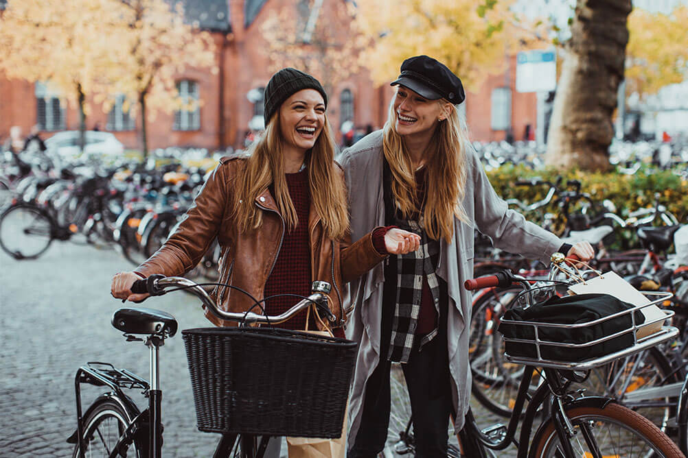 Two young women lead their bikes through the city happy to reduce their carbon footprint