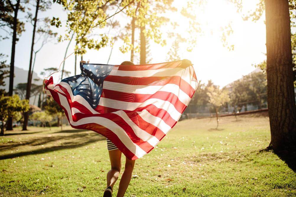 woman-celebrating-with-american-flag-through-sunny-park