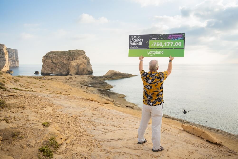 Gozo casino winner Lottoland winner holding up cheque facing the sea